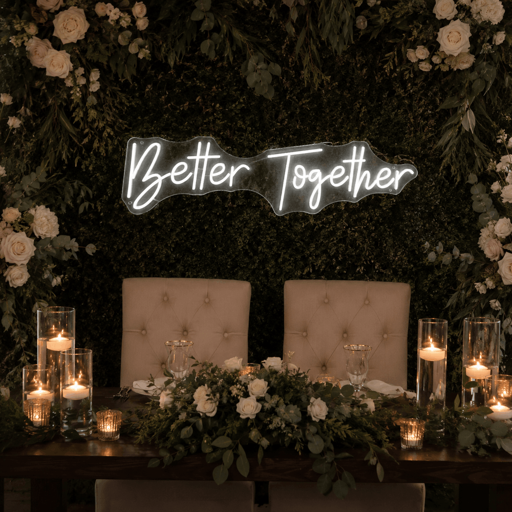 Better Together LED neon sign displayed above a wedding sweetheart table with candles, greenery, and white floral decor.
