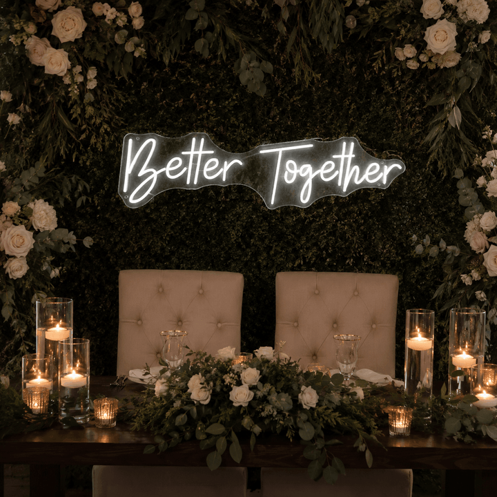 Better Together LED neon sign displayed above a wedding sweetheart table with candles, greenery, and white floral decor.