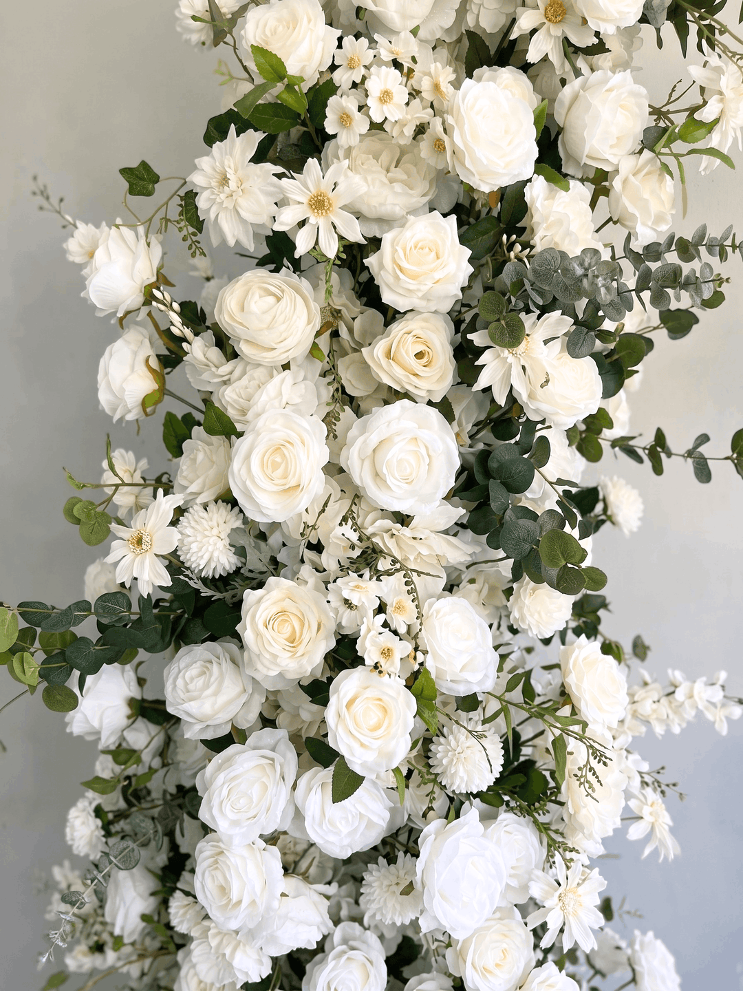 Detailed macro photograph of the Bianca silk floral arch, showcasing premium high-density white roses, hydrangeas, and trailing eucalyptus greenery with life-like texture.
