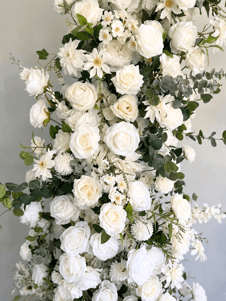 Detailed macro photograph of the Bianca silk floral arch, showcasing premium high-density white roses, hydrangeas, and trailing eucalyptus greenery with life-like texture.