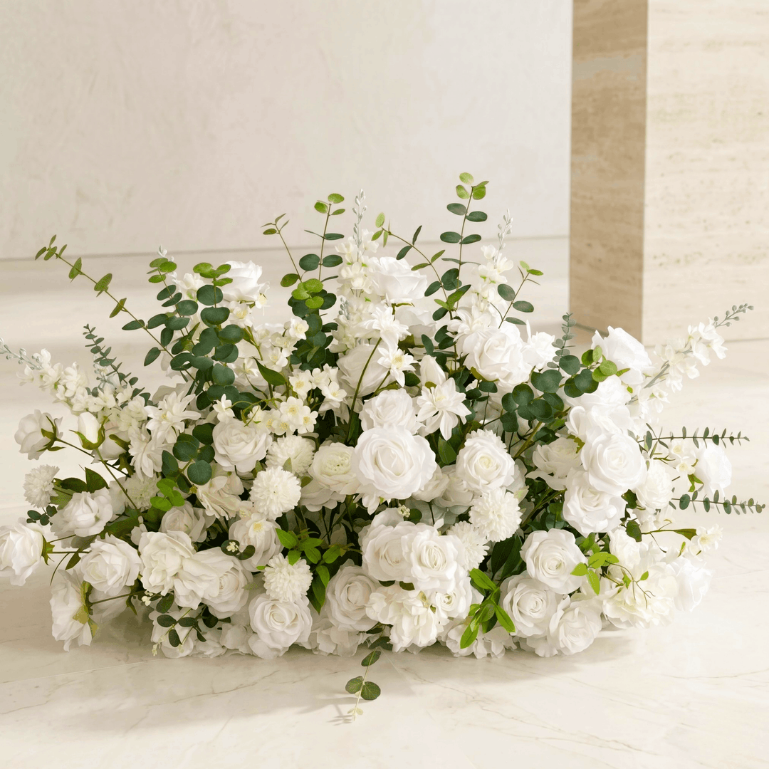 White rose and eucalyptus wedding aisle flower meadow arrangement sitting on a light floor.