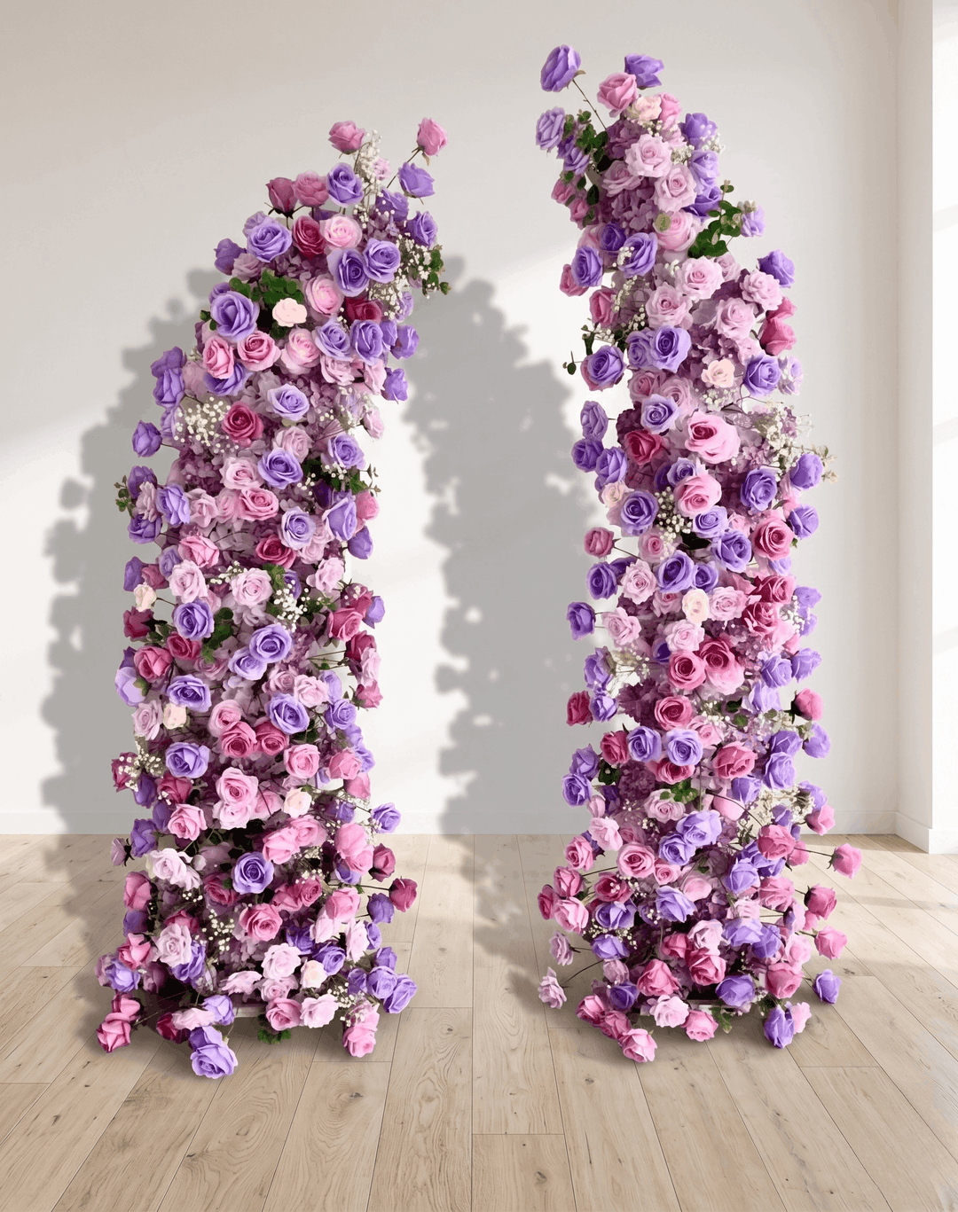 Two floral arches decorated with pink and purple flowers on a wooden floor.