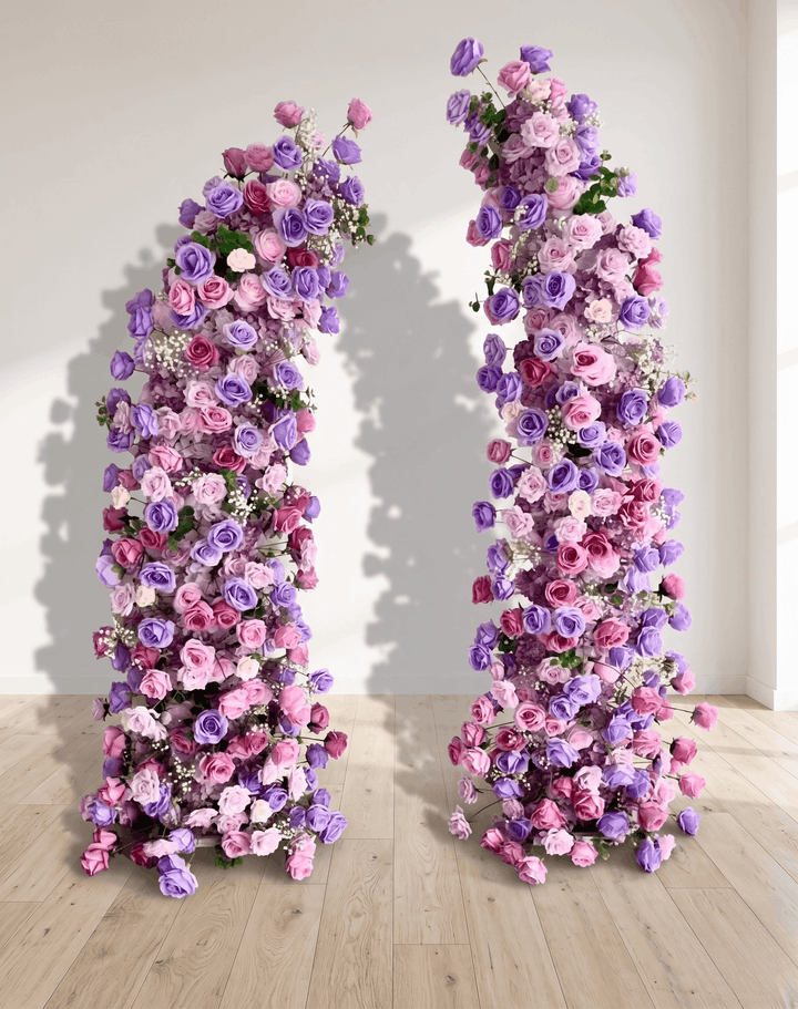 Two floral arches decorated with pink and purple flowers on a wooden floor.