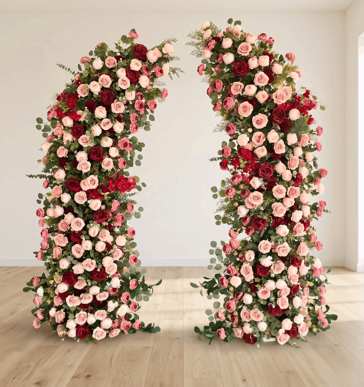 Two tall floral arrangements in red, pink, and green on a wooden floor.