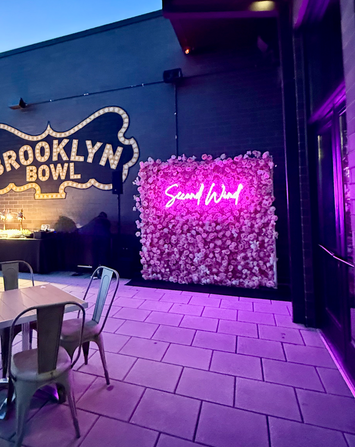 Pink rose and white carnation silk flower wall backdrop with custom illuminated neon sign setup for an outdoor evening event