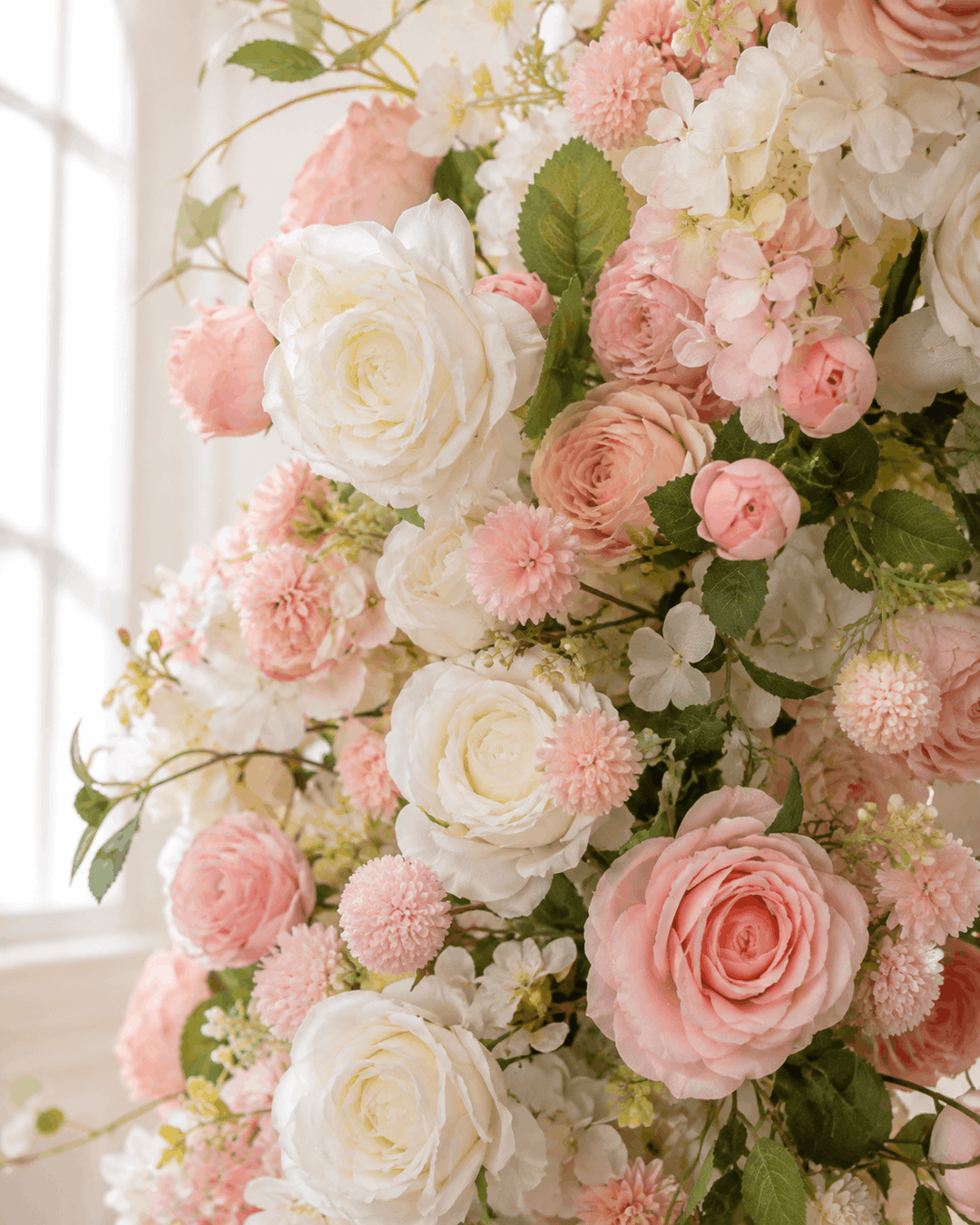 Close-up of pink and white silk faux flowers with roses and greenery on a floral wedding arch