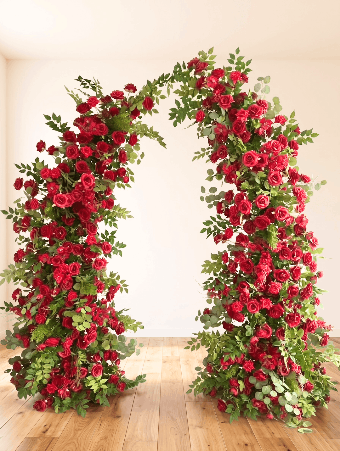 Floral arch made of red roses and greenery on a wooden floor.