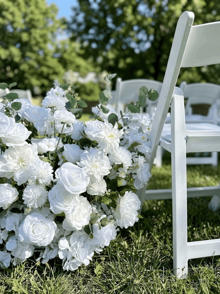Ground-level floral meadow aisle runner made with white silk roses, hydrangeas, and greenery next to a white wooden ceremony chair.