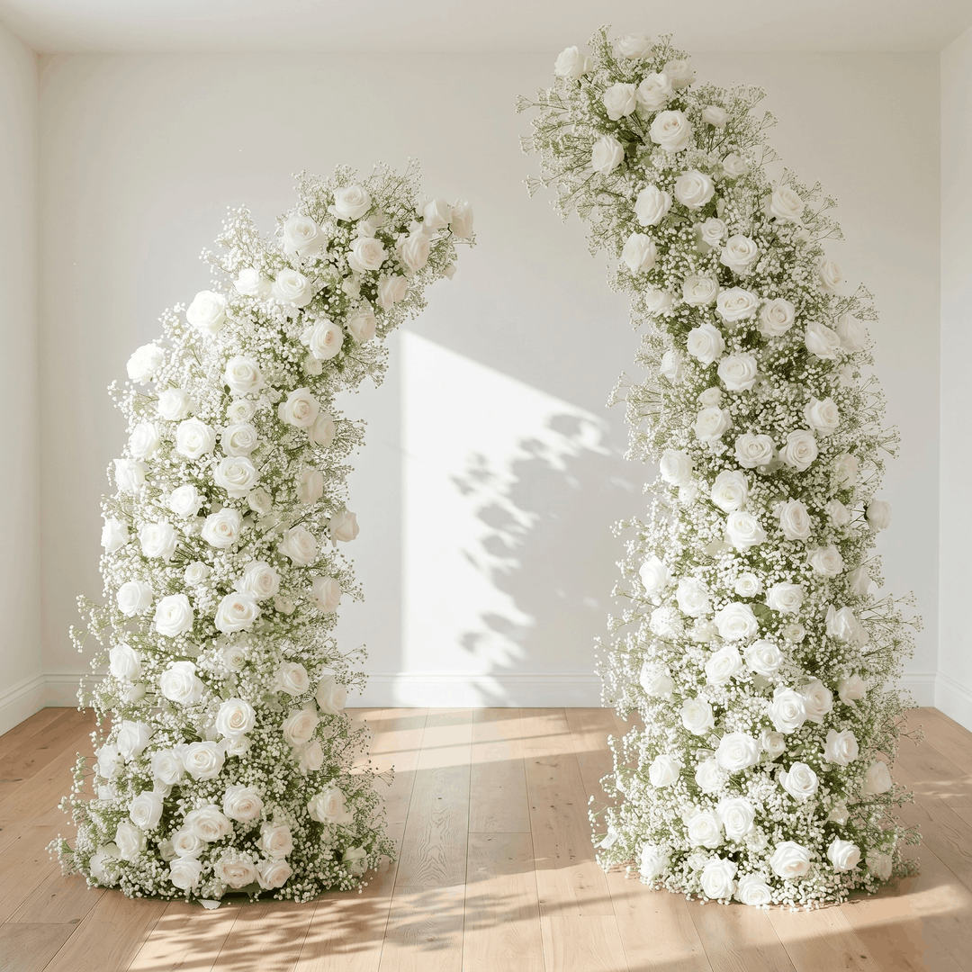 Floral arches decorated with white roses and baby's breath in a room with wooden flooring.