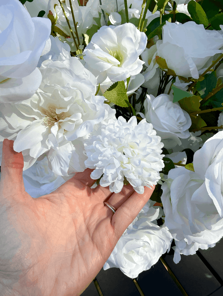 Close-up hand detail showing the lush texture and realistic white silk rose, peony, and dahlia flowers of a floral meadow aisle runner.